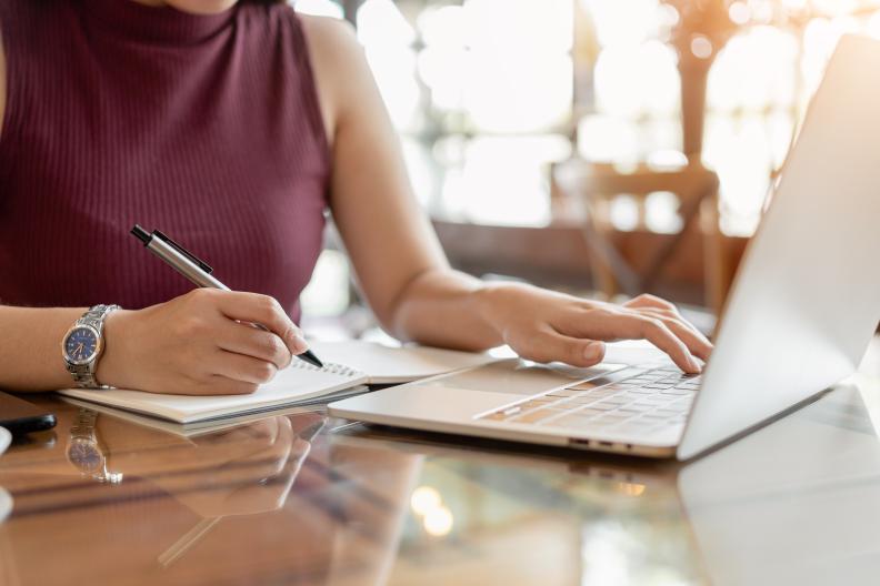 Person sitzt am Schreibtisch,arbeitet am Laptop und hat einen Stift in der Hand