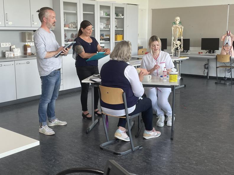 Vier Menschen sprechen miteinander in einem Raum, in dem medizinische Gegenstände sind.