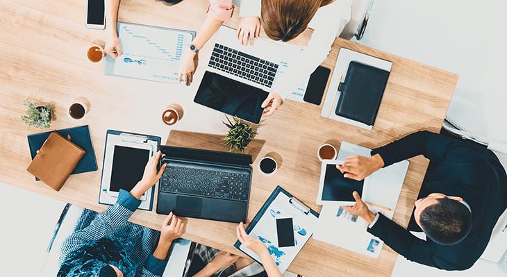 Schreibtisch mit drei Personen, die an Laptops arbeiten, aus der Vogelperspektive