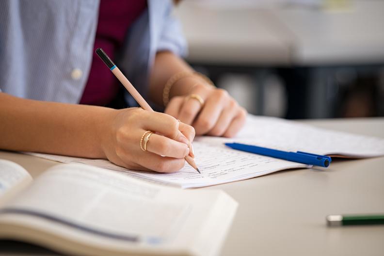 Es sind Hände zu sehen, die mit einem Stift in ein Heft schreiben