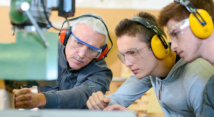 Ausbilder in Schreinerei mit zwei Auszubildenden bei Arbeit an Maschine
