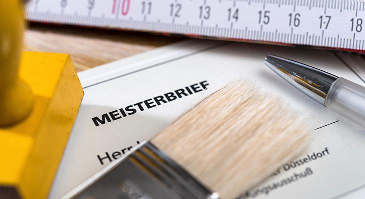Dokument mit Titel Meisterbrief auf Schreibtisch neben Stempel und Zollstock