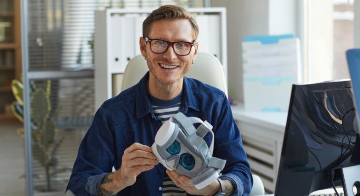 Mann in Büro am PC sitzend mit VR-Brille in der Hand