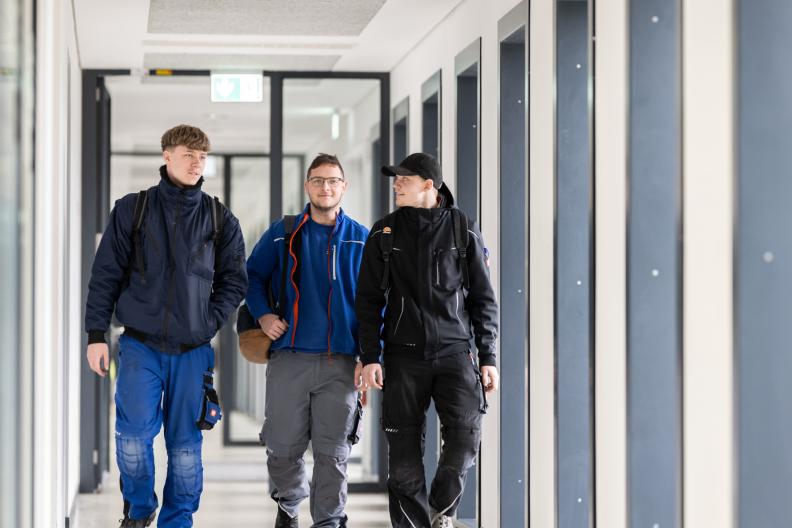 Drei Auszubildende gehen nebeneinander durch einen Flur