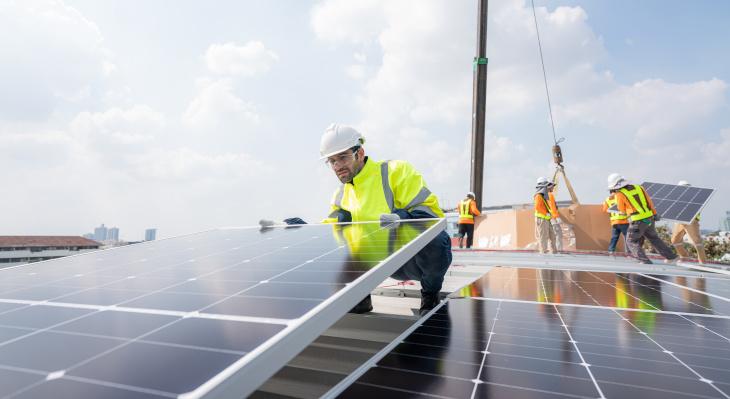 Mann in Arbeitskleidung installiert PV-Anlage auf Dach