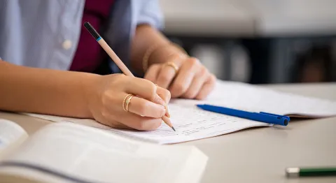 Es sind Hände zu sehen, die mit einem Stift in ein Heft schreiben